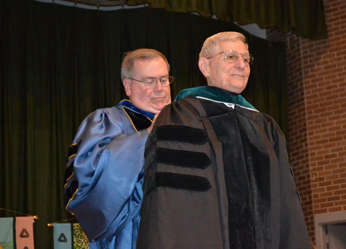 Delta State University President Dr. John Hilpert (back) hoods retired State Senator and Delta State alumnus Bob M. Dearing, bestowing one of the university’s highest honors – an honorary Doctor of Public Service degree.